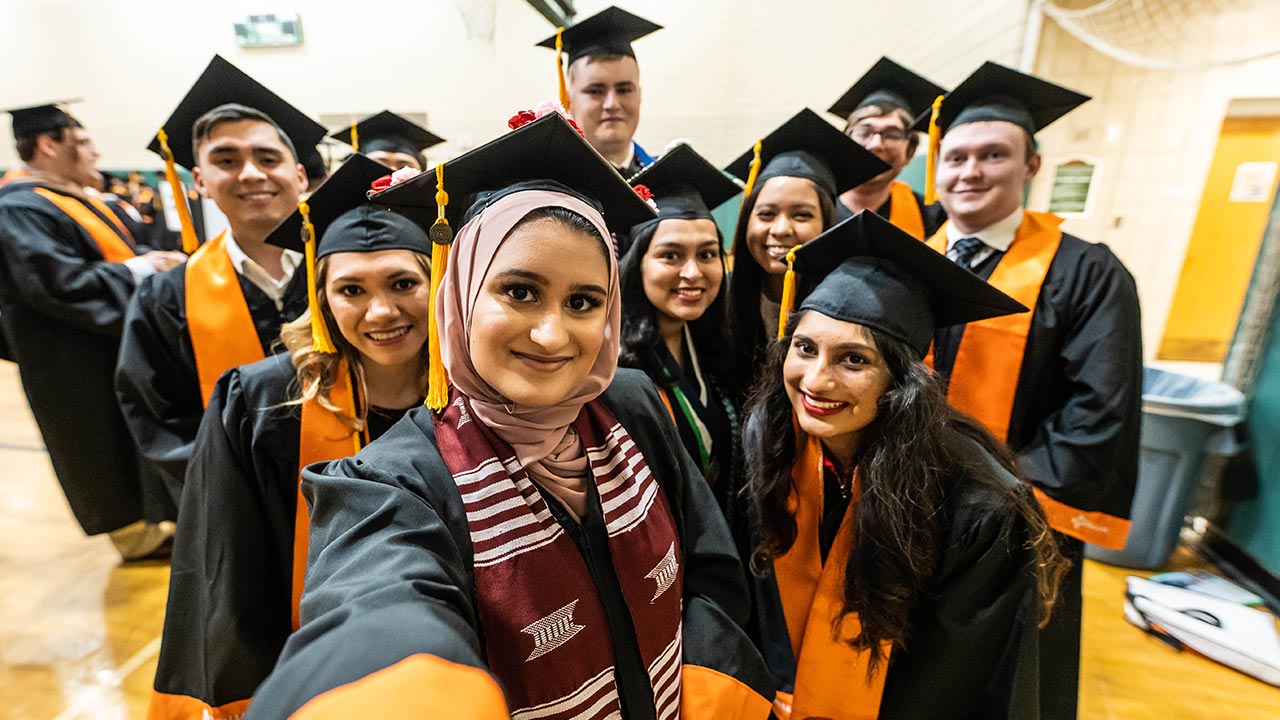 Recent grads take a selfie in their caps and gowns.
