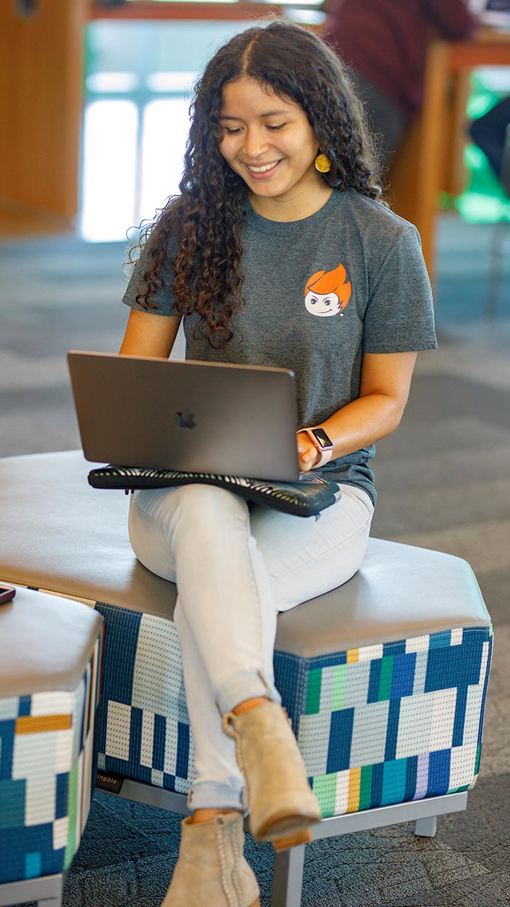 Student wearing a temoc shirt works on a laptop on campus.
